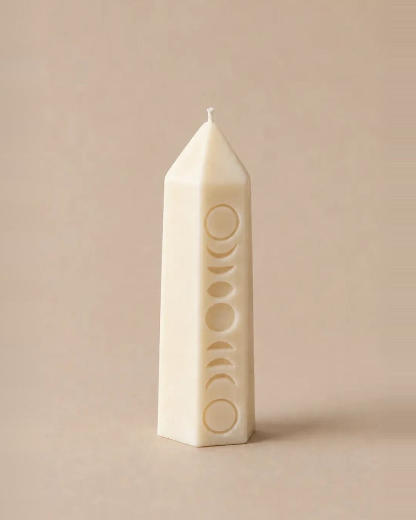 The Cycle, an ivory soy wax crystal candle carved with the phases of the moon, on a warm beige backdrop